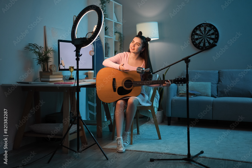 Female student with guitar and microphone streaming at home in evening