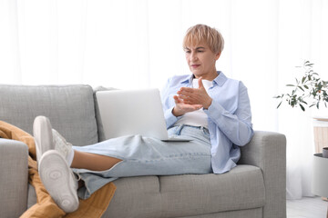 Wall Mural - Upset mature deaf mute woman video chatting in sign language on sofa at home