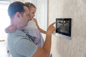 Daughter in her father using tablet panel application for control smart home living. Wireless device controller for home automation IoT on the wall