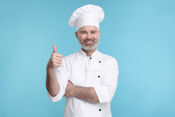 Wall Mural - Happy chef in uniform showing thumbs up on light blue background