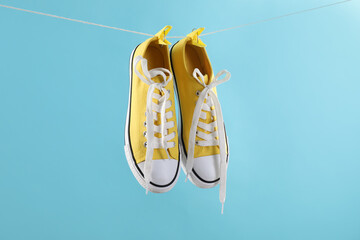 Wall Mural - Stylish sneakers drying on washing line against light blue background