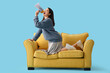 © Pixel-Shot - Young woman shouting into megaphone on yellow sofa against blue background
