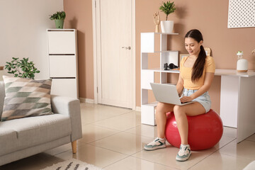 Sticker - Young Asian woman using laptop on fitball at home