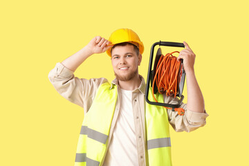 Wall Mural - male contractor with extension cord reel on yellow background