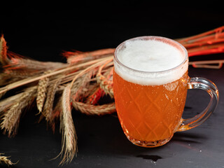 Wall Mural - A mug of cold wheat beer on a black table . Ears of wheat