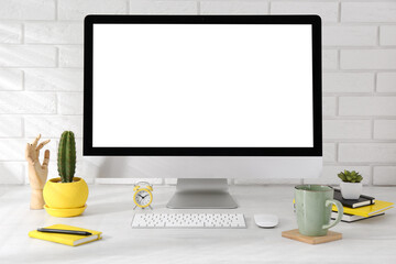 Wall Mural - Office workplace with computer, stationery, cup and houseplants on light table near white brick wall