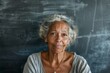 © Studium L&M - Portrait of wise senior mix race female teacher with warm smile in classroom; chalkboard background, educational themes.