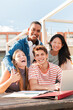 © Jose Calsina - Vertical. Diverse Group of Males and Females Students Gazing at the Camera While Collaboratively Studying Using a Laptop on the University Campus. Multiracial teenagers smiling and doing the homeworks