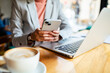 © Marko Geber - Close up of a businesswoman using smartphone and laptop in a cafe