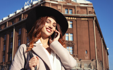 smiling young woman calling and talking on smartphone in the autumn city