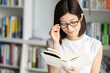 © amanaimages - 本棚の前でメガネをかけて本を読んでいる女性