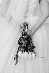 Wall Mural - a bride in a white dress holds a wedding bouquet of white roses behind her back black and white photo
