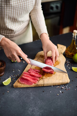 Wall Mural - Woman cut tuna steak into slices on a wooden cutting board at domestic kitchen