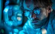 © imagineRbc - A man wearing glasses is focused on examining an object illuminated by blue light, showing curiosity and concentration