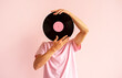 © dvulikaia - Portrait of man in pink shirt holding vinyl record near his face on pink background.