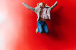 © Westend61 - Cheerful girl jumping with arms raised near red wall
