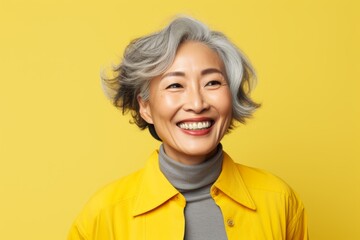 Wall Mural - Portrait of a cheerful asian woman in her 50s smiling at the camera in front of pastel yellow background