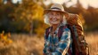 © nicole - Elderly woman enjoying an active lifestyle, walking in nature with a smile. She is sporting a backpack and hat, embodying outdoor activity, health, and happiness