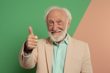 Wall Mural - Portrait of a jovial man in his 80s showing a thumb up in front of solid pastel color wall