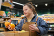 © Mediaphotos - Waist up portrait of smiling young woman with disability working in supermarket sorting fresh fruits and produce