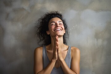 Poster - Portrait of a blissful woman in her 30s joining palms in a gesture of gratitude in bare concrete or plaster wall
