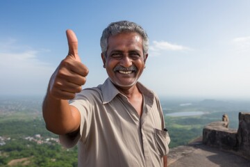 Portrait of a tender indian man in his 50s showing a thumb up in bare concrete or plaster wall