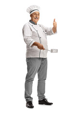 Wall Mural - Mature male chef holding a utensil and showing a thumb up gesture