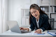 © Wasana - A woman is sitting at a desk with a laptop and a stack of papers. She is typing on the laptop and she is focused on her work. Concept of productivity and concentration