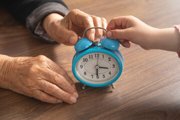 Hands of elderly female and young girl holding clock.