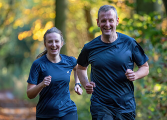 Wall Mural - A man and woman in their late thirties, dressed for running with dark blue t-shirts, wearing black shorts or leggings, smiling as they run side by side through the park on an autumn morning