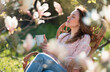 © Kien - A woman sitting in an outdoor chair with her eyes closed, holding a coffee mug and enjoying the spring sunshine in her home garden.