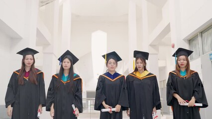 Wall Mural - A group of five women in graduation gowns are standing in a hallway. They are all holding their graduation certificates