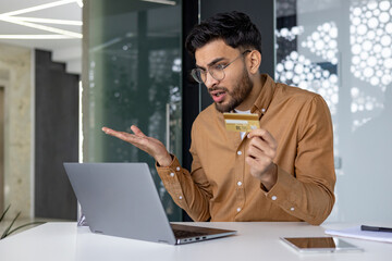 Man questioning online banking transaction while holding credit card at desk