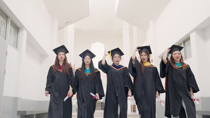 Wall Mural - A group of five women in graduation gowns walk down a hallway. Scene is celebratory and proud, as the women are wearing their graduation gowns and holding their diplomas