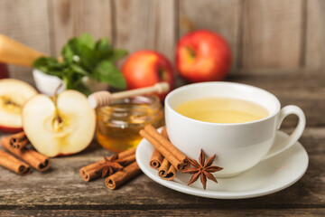 Wall Mural - Fragrant hot tea with cinnamon stick and anise on a textured wooden background. A cup of hot tea with honey, lemon, mint and apples. Spicy tea with spices. Immunity tea. Health concept.Copy space.