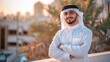 © Viktoriia Kan - A young Saudi man stands with his arms crossed and smiles, dressed in traditional red and white. Confident Arab businessman posing for the camera outdoors.