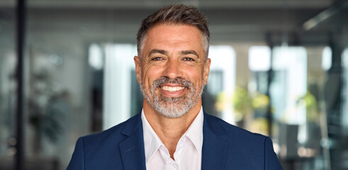 Headshot close up banner portrait of indian or latin confident mature good looking middle age, male ceo businessman in suit on office background. Handsome hispanic senior business man smile at camera.