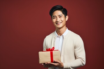 Wall Mural - Portrait of a happy asian man in his 20s holding a gift isolated on blank studio backdrop