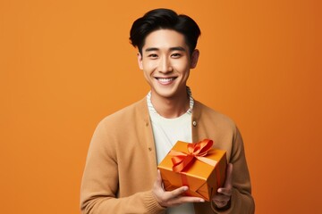 Wall Mural - Portrait of a happy asian man in his 20s holding a gift over blank studio backdrop