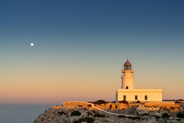 Sticker - vertical view of the Cap de Cavalleria Lighthouse on Menorca at sunset with a full moon rising