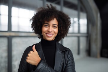 Wall Mural - Portrait of a blissful afro-american woman in her 40s showing a thumb up over empty modern loft background