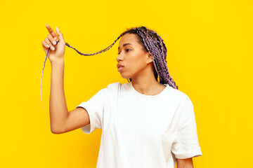 Wall Mural - young african american woman with dreadlocks pointing with hand up on yellow isolated background, girl with unique hairstyle and colored braids touching and pointing