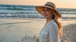 © PeopleWorker - Beautiful attractive blonde woman model standing walking at beach wearing hat, happy travel concept