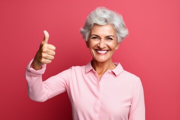 Wall Mural - Portrait of a cheerful woman in her 60s showing a thumb up isolated on bare monochromatic room