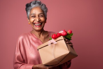 Wall Mural - Portrait of a cheerful indian woman in her 60s holding a gift while standing against plain cyclorama studio wall