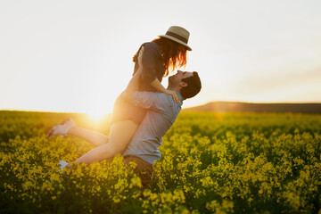 Man, lift and woman with sunset for love in nature, care and bonding for memory on field in countryside. Couple, embrace and vacation with smile, connection and excited with floral plants in spring