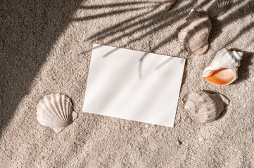 Wall Mural - Empty paper card mockup and sea shells and conch on beige sand texture background with tropical palm tree leaves sunlight shadow