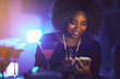 © peopleimages.com - Phone, smile and black woman at nightclub, party or celebration event on social media. Smartphone, bar and happy girl at rave with drinks at pub on internet app, typing and scroll for online dating