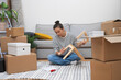 © olga_demina - Rental Comfort: Woman tenant sits on the floor, assembling self-assembly shelf amidst moving carton boxes and furniture, making her new place feel like home