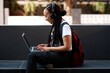 © peopleimages.com - Woman, student and headset with laptop outside, typing and online classes for elearning or education. University, learner and website research for assignment, listening and podcast or school project